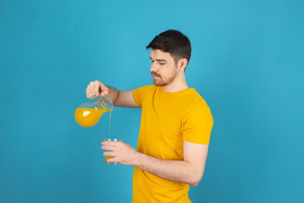 Junger gutaussehender Mann, der auf einem Blau Saft in das Glas gießt.