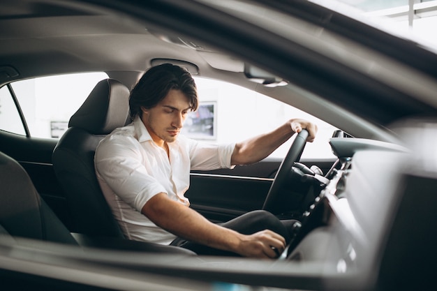 Junger gutaussehender Mann, der ein Auto in einem Autosalon wählt