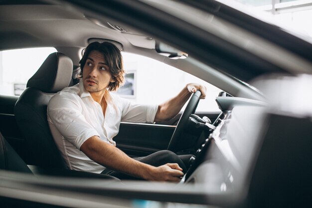 Junger gutaussehender Mann, der ein Auto in einem Autosalon wählt