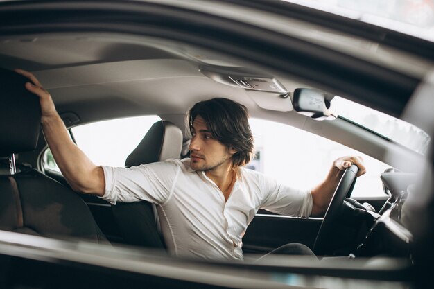 Junger gutaussehender Mann, der ein Auto in einem Autosalon wählt