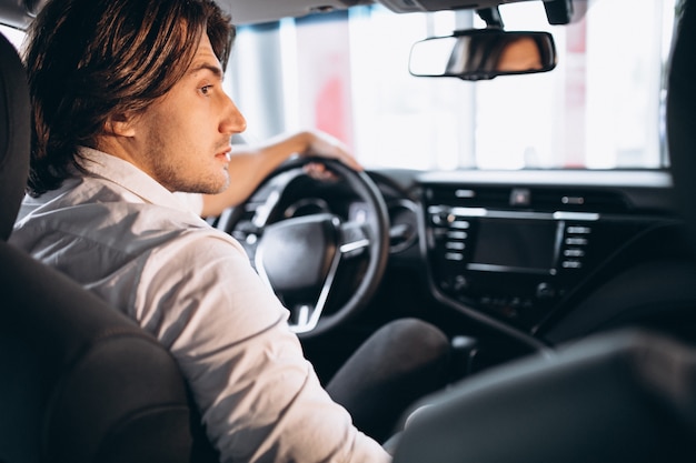 Junger gutaussehender Mann, der ein Auto in einem Autosalon wählt