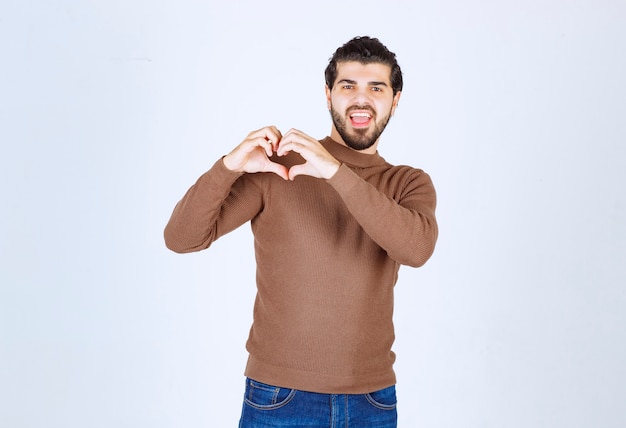 Junger gutaussehender Mann, der Freizeitkleidung trägt und lächelt und Herzsymbolform mit den Händen tut. Foto in hoher Qualität