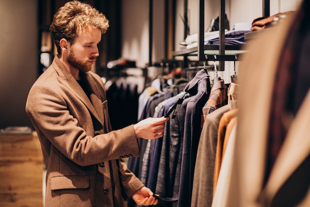 Junger gutaussehender Mann, der Kleidung am Shop wählt