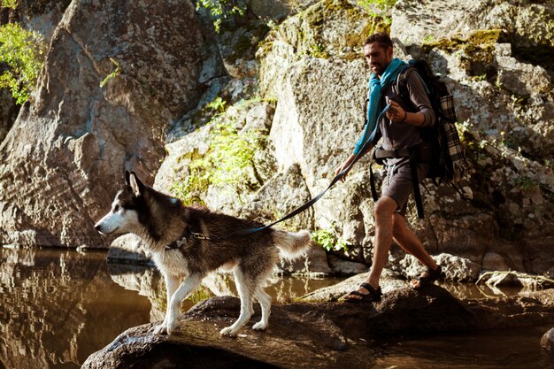 Junger gutaussehender Mann, der mit Huskys Hund in der Schlucht nahe Wasser geht