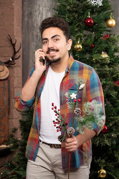 Junger gutaussehender Mann, der mit Telefon vor Weihnachtsbaum spricht.