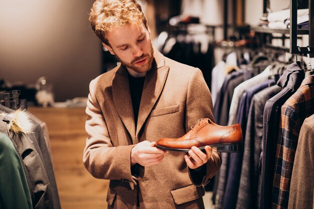 Junger gutaussehender Mann, der Schuhe an einem Shop wählt