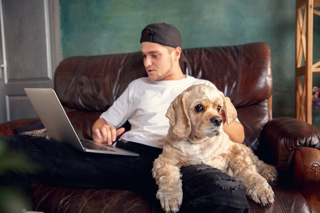 Junger gutaussehender Mann, der zu Hause mit seinem süßen Hund sitzt und arbeitet.