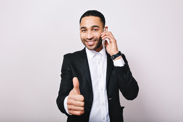 Junger gutaussehender Mann des stilvollen Porträts im weißen Hemd, schwarze Jacke lächelnd, am Telefon sprechend. Erfolg, großartige Arbeit, Treffen, Lächeln, Ausdruck wahrer positiver Emotionen.