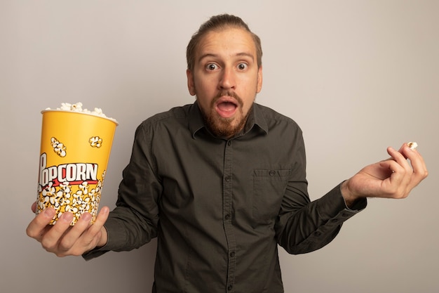 Junger gutaussehender Mann im grauen Hemd, das Eimer mit Popcorn zeigt verwirrte Achselzucken