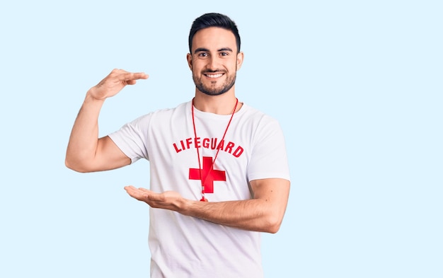 Junger gutaussehender Mann in Rettungsschwimmeruniform gestikuliert mit Händen, die ein großes und großes Schild und ein Maßsymbol zeigen. lächelnd in die Kamera schauend. Messkonzept.