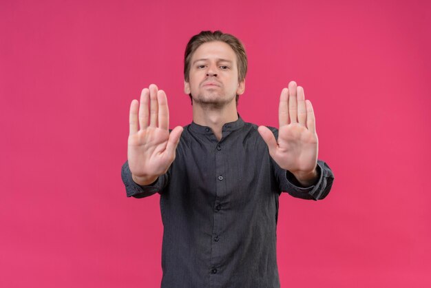 Junger gutaussehender Mann mit ernstem Gesicht und offenen Händen, die Stoppschild über rosa Wand stehen lassen