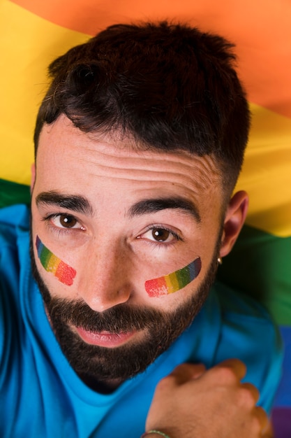 Junger gutaussehender Mann mit LGBT-Regenbogenflagge auf Gesicht