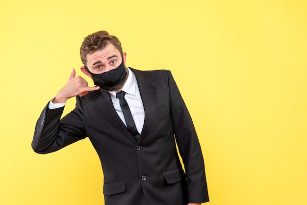 Kostenloses Foto junger händler mit medizinischer maske, die die kontaktgeste geste auf gelb zeigt