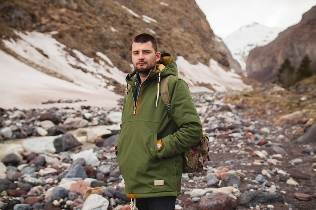 Junger Hipster-Mann, der durch den Fluss, wilde Natur, Winterferien wandert