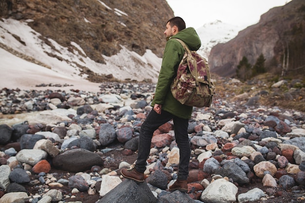 Junger Hipster-Mann, der durch den Fluss, wilde Natur, Winterferien wandert