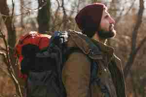 Kostenloses Foto junger hipster-mann, der mit rucksack im herbstwald reist und warme jacke und hut trägt