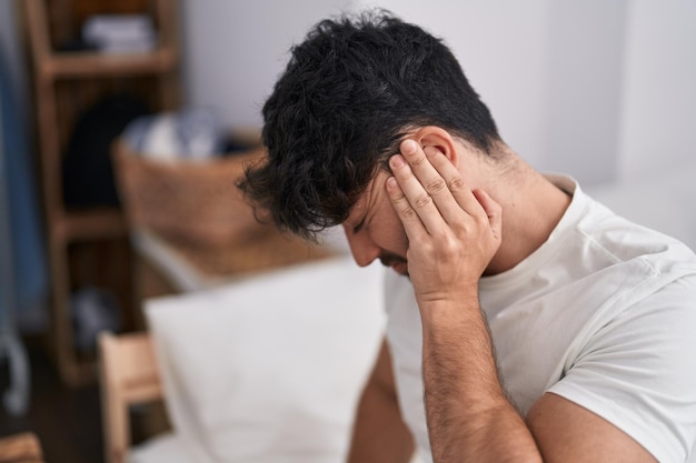 Junger hispanischer Mann, der unter Rückenschmerzen leidet, sitzt im Schlafzimmer auf dem Bett