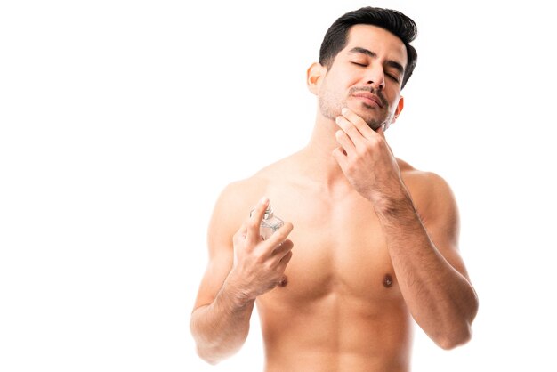 Junger hispanischer Mann mit Bart, der etwas Eau de Cologne auf seinen Hals sprüht