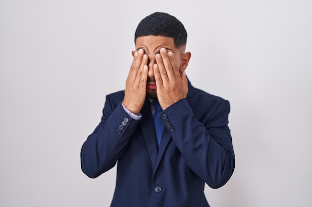 Junger hispanischer Mann mit Business-Anzug und Krawatte, der die Augen wegen Müdigkeit und Kopfschmerzen, schläfriger und müder Ausdruck reibt. Sehproblem