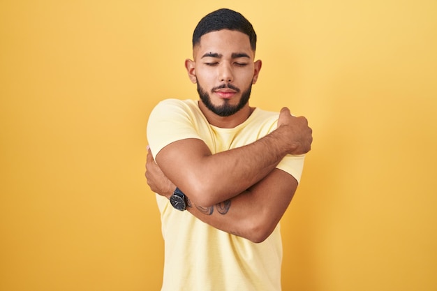 Kostenloses Foto junger hispanischer mann steht vor gelbem hintergrund, umarmt sich glücklich und positiv und lächelt selbstbewusst. selbstliebe und selbstfürsorge