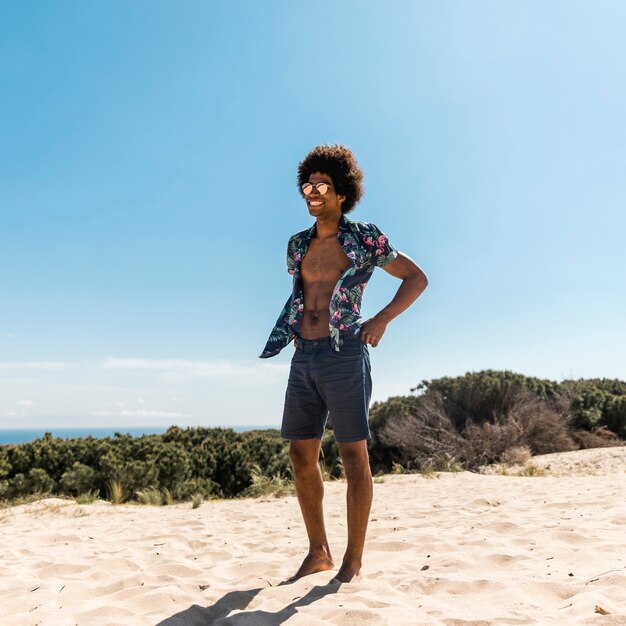 Junger hübscher Afroamerikanermann, der auf Strand aufwirft