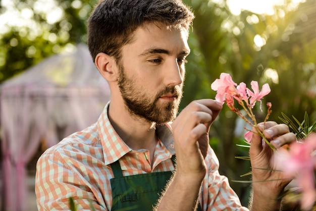 Junger hübscher fröhlicher Gärtner, der lächelt und sich um Blumen kümmert