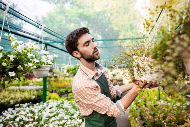 Junger hübscher fröhlicher Gärtner, der lächelt und sich um Blumen kümmert