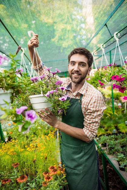 Junger hübscher fröhlicher Gärtner, der lächelt und sich um Blumen kümmert