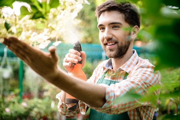 Kostenloses Foto junger hübscher fröhlicher gärtner, der lächelt, wässert und sich um blumen kümmert