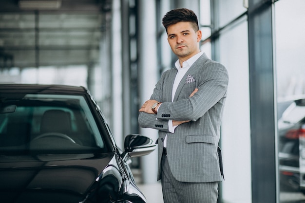 Junger hübscher Geschäftsmann, der ein Auto in einem Autosalon wählt