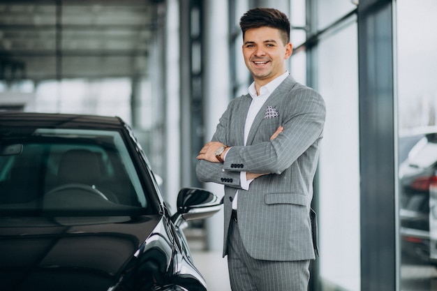 Junger hübscher Geschäftsmann, der ein Auto in einem Autosalon wählt