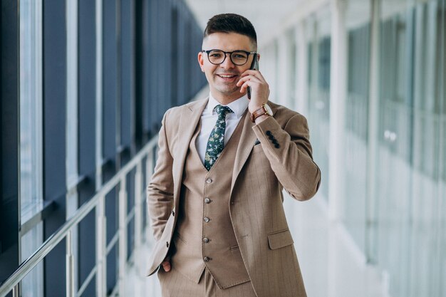 Junger hübscher Geschäftsmann, der mit Telefon im Büro steht