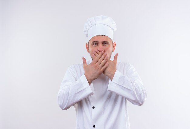Junger hübscher Koch in der Kochuniform, die Mund mit den Händen lokalisiert auf weißem Raum schließt