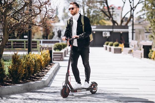 Junger hübscher Mann, der auf Roller im Park reitet