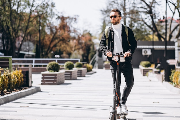 Junger hübscher Mann, der auf Roller im Park reitet