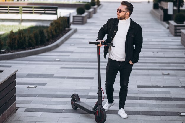 Junger hübscher Mann, der auf Roller im Park reitet