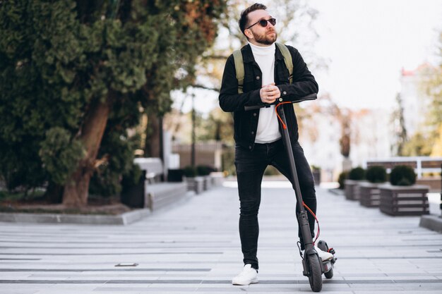 Junger hübscher Mann, der auf Roller im Park reitet