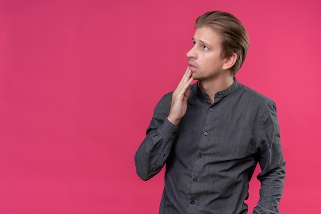 Junger hübscher Mann, der beiseite mit nachdenklichem Ausdruck auf Gesicht steht, das über rosa Wand steht