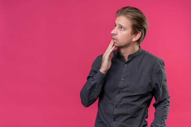 Junger hübscher Mann, der beiseite mit nachdenklichem Ausdruck auf Gesicht steht, das über rosa Wand steht