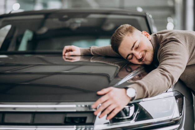 Junger hübscher Mann, der ein Auto in einem Autoausstellungsraum umarmt