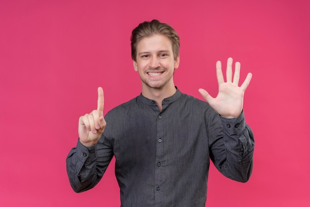 Junger hübscher Mann, der mit den Fingern Nummer sechs zeigt und zeigt