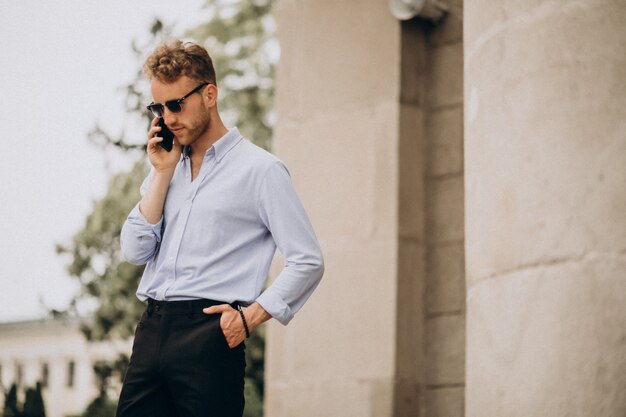 Junger hübscher Mann, der Telefon draußen in der Straße benutzt