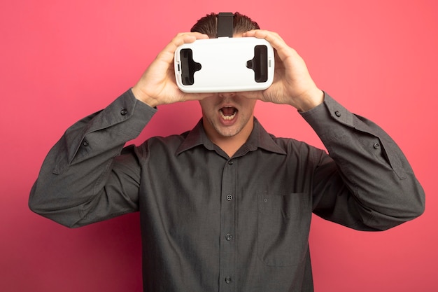 Junger hübscher Mann im grauen Hemd mit der Brille der virtuellen Realität erstaunt und überrascht