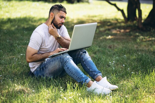 Junger hübscher Student mit Laptop in einem Universitätspark