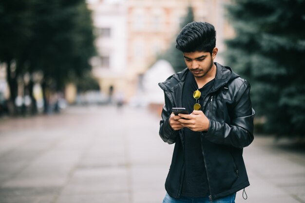 Junger indischer Mann gekleidet im trendigen Outfit, das Informationen von sozialen Netzwerken überwacht