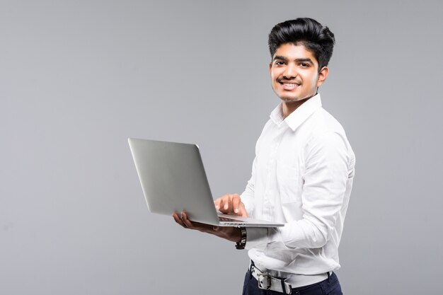 Junger indischer Mann mit Laptop auf grauer Wand