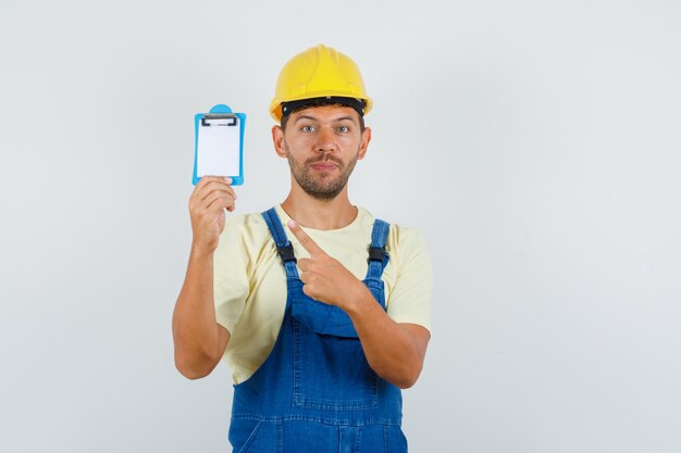 Junger Ingenieur in Uniform, die auf Mini-Zwischenablage zeigt, Vorderansicht.