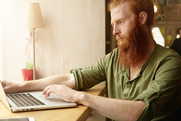 Junger Ingwermann, der Laptop im Café verwendet