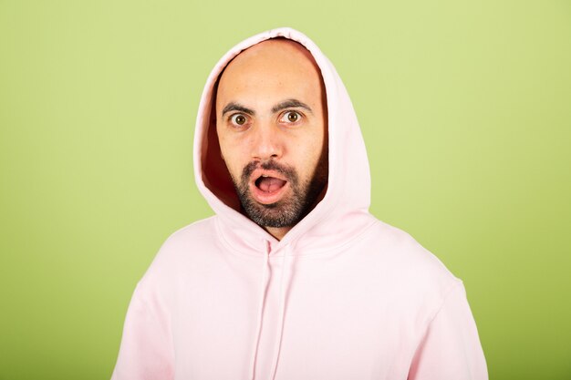 Junger kahler kaukasischer Mann im rosa Kapuzenpulli isoliert, sieht mit Überraschung und erstauntem Ausdruck schockiert aus