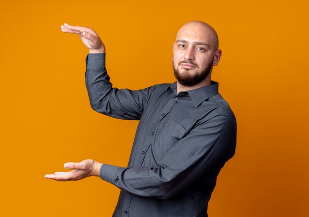 Junger kahlköpfiger Callcenter-Mann, der Größe lokalisiert auf orange Hintergrund mit Kopienraum zeigt